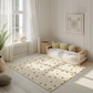 Kinderteppich "Bienchen Summ" von spielzwerg. Ambientebild von einem hellen, freundlichen Kinderzimmer mit weißen Holzwänden und hellem Holzboden. In der Ecke steht ein niedriges Holzbett mit weißen Decken und hellgrünen Kissen. Davor liegt der Teppich. Links steht ein kleines Holzspielzeugrad am Fenster mit weißen Vorhängen. An der Wand hängt ein gerahmtes Bild mit einem dezenten, kreisförmigen Muster. RUG-00084-XL, RUG-00084-L.