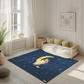 Kinderteppich "Kim Katze" von spielzwerg. Ambientebild von einem hellen, freundlichen Kinderzimmer mit weißen Holzwänden und hellem Holzboden. In der Ecke steht ein niedriges Holzbett mit weißen Decken und hellgrünen Kissen. Davor liegt der Teppich. Links steht ein kleines Holzspielzeugrad am Fenster mit weißen Vorhängen. An der Wand hängt ein gerahmtes Bild mit einem dezenten, kreisförmigen Muster. RUG-00144-XL, RUG-00144-L.