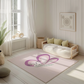 Kinderteppich "Schmetti" von spielzwerg. Ambientebild von einem hellen, freundlichen Kinderzimmer mit weißen Holzwänden und hellem Holzboden. In der Ecke steht ein niedriges Holzbett mit weißen Decken und hellgrünen Kissen. Davor liegt der Teppich. Links steht ein kleines Holzspielzeugrad am Fenster mit weißen Vorhängen. An der Wand hängt ein gerahmtes Bild mit einem dezenten, kreisförmigen Muster. RUG-00064-XL, RUG-00064-L.
