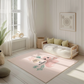 Kinderteppich "Mia Dino" von spielzwerg. Ambientebild von einem hellen, freundlichen Kinderzimmer mit weißen Holzwänden und hellem Holzboden. In der Ecke steht ein niedriges Holzbett mit weißen Decken und hellgrünen Kissen. Davor liegt der Teppich. Links steht ein kleines Holzspielzeugrad am Fenster mit weißen Vorhängen. An der Wand hängt ein gerahmtes Bild mit einem dezenten, kreisförmigen Muster. RUG-00112-XL, RUG-00112-L.