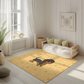 Kinderteppich "Danny Dackel" von spielzwerg. Ambientebild von einem hellen, freundlichen Kinderzimmer mit weißen Holzwänden und hellem Holzboden. In der Ecke steht ein niedriges Holzbett mit weißen Decken und hellgrünen Kissen. Davor liegt der Teppich. Links steht ein kleines Holzspielzeugrad am Fenster mit weißen Vorhängen. An der Wand hängt ein gerahmtes Bild mit einem dezenten, kreisförmigen Muster. RUG-00146-XL, RUG-00146-L.