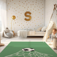 Kinderteppich "Volltreffer" von spielzwerg. Ambientebild von einem hellen Kinderzimmer mit weißem Holzboden und weißen Wänden, dekoriert mit goldenen Dreiecken und einem großen goldenen Buchstaben 'S'. Links steht ein gemütlicher Sessel mit Kissen und Decke, daneben eine goldene Stehlampe. In der Mitte liegt der Teppich. Rechts sitzt ein lachender Junge in einem weißen Spielzelt mit goldenen Punkten. Im Hintergrund ein schlichtes Bett mit weißer Decke und goldenen Akzenten. RUG-00079-XL, RUG-00079-L.