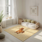 Kinderteppich "Pia Pony" von spielzwerg. Ambientebild von einem hellen, freundlichen Kinderzimmer mit weißen Holzwänden und hellem Holzboden. In der Ecke steht ein niedriges Holzbett mit weißen Decken und hellgrünen Kissen. Davor liegt der Teppich. Links steht ein kleines Holzspielzeugrad am Fenster mit weißen Vorhängen. An der Wand hängt ein gerahmtes Bild mit einem dezenten, kreisförmigen Muster. RUG-00147-XL, RUG-00147-L.