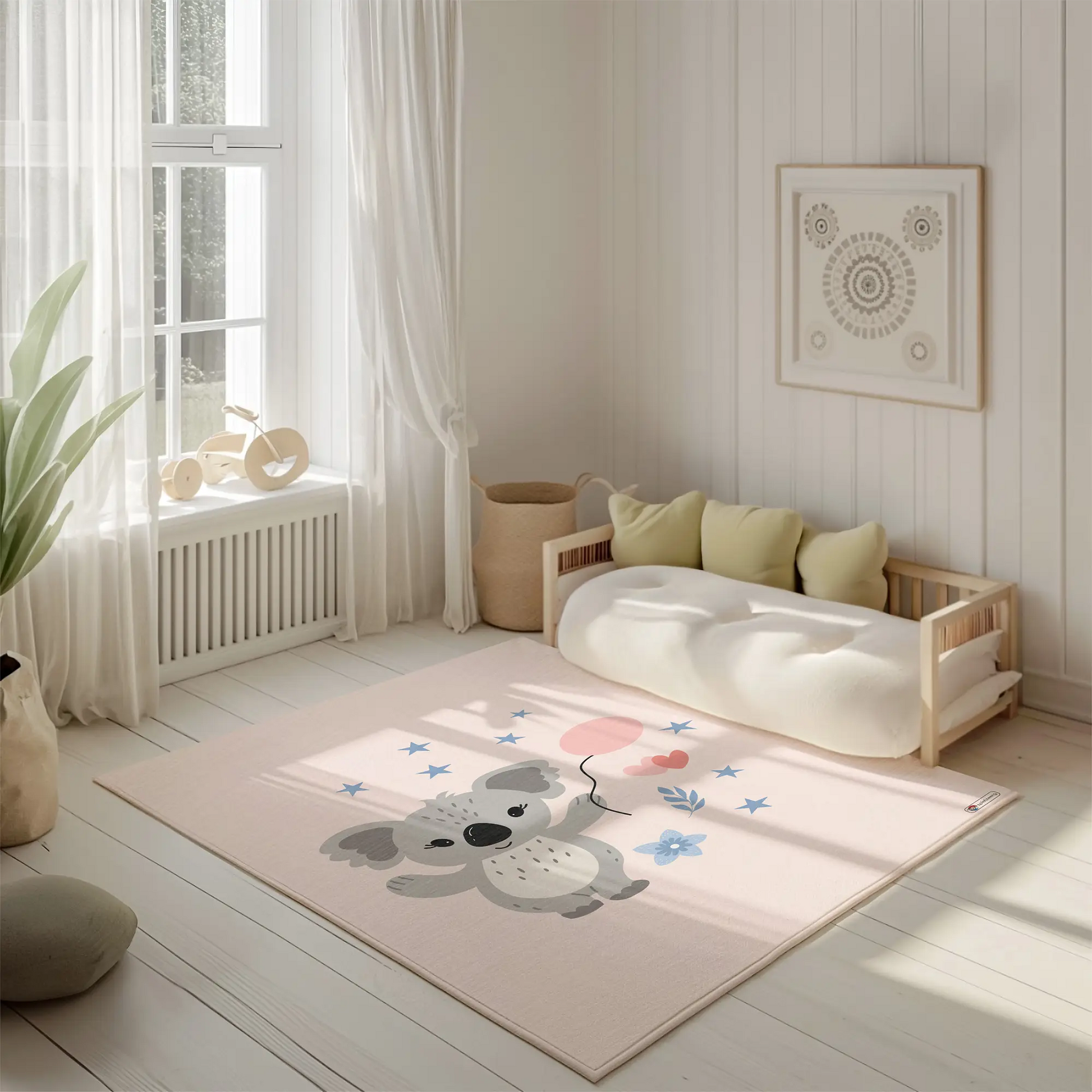 Kinderteppich "Cora Koala" von spielzwerg. Ambientebild von einem hellen, freundlichen Kinderzimmer mit weißen Holzwänden und hellem Holzboden. In der Ecke steht ein niedriges Holzbett mit weißen Decken und hellgrünen Kissen. Davor liegt der Teppich. Links steht ein kleines Holzspielzeugrad am Fenster mit weißen Vorhängen. An der Wand hängt ein gerahmtes Bild mit einem dezenten, kreisförmigen Muster. RUG-00022-XL, RUG-00022-L.