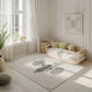 Kinderteppich "Koala-Gesicht" von spielzwerg. Ambientebild von einem hellen, freundlichen Kinderzimmer mit weißen Holzwänden und hellem Holzboden. In der Ecke steht ein niedriges Holzbett mit weißen Decken und hellgrünen Kissen. Davor liegt der Teppich. Links steht ein kleines Holzspielzeugrad am Fenster mit weißen Vorhängen. An der Wand hängt ein gerahmtes Bild mit einem dezenten, kreisförmigen Muster. RUG-00191-XL, RUG-00191-L.