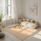 Kinderteppich "Abu Affe" von spielzwerg. Ambientebild von einem hellen, freundlichen Kinderzimmer mit weißen Holzwänden und hellem Holzboden. In der Ecke steht ein niedriges Holzbett mit weißen Decken und hellgrünen Kissen. Davor liegt der Teppich. Links steht ein kleines Holzspielzeugrad am Fenster mit weißen Vorhängen. An der Wand hängt ein gerahmtes Bild mit einem dezenten, kreisförmigen Muster. RUG-00128-XL, RUG-00128-L.