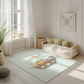 Kinderteppich "Arche Noah" von spielzwerg. Ambientebild von einem hellen, freundlichen Kinderzimmer mit weißen Holzwänden und hellem Holzboden. In der Ecke steht ein niedriges Holzbett mit weißen Decken und hellgrünen Kissen. Davor liegt der Teppich. Links steht ein kleines Holzspielzeugrad am Fenster mit weißen Vorhängen. An der Wand hängt ein gerahmtes Bild mit einem dezenten, kreisförmigen Muster. RUG-00003-XL, RUG-00003-L.