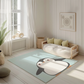 Kinderteppich "Pingu" von spielzwerg. Ambientebild von einem hellen, freundlichen Kinderzimmer mit weißen Holzwänden und hellem Holzboden. In der Ecke steht ein niedriges Holzbett mit weißen Decken und hellgrünen Kissen. Davor liegt der Teppich. Links steht ein kleines Holzspielzeugrad am Fenster mit weißen Vorhängen. An der Wand hängt ein gerahmtes Bild mit einem dezenten, kreisförmigen Muster. RUG-00185-XL, RUG-00185-L.