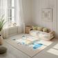 Kinderteppich "Cindy" von spielzwerg. Ambientebild von einem hellen, freundlichen Kinderzimmer mit weißen Holzwänden und hellem Holzboden. In der Ecke steht ein niedriges Holzbett mit weißen Decken und hellgrünen Kissen. Davor liegt der Teppich. Links steht ein kleines Holzspielzeugrad am Fenster mit weißen Vorhängen. An der Wand hängt ein gerahmtes Bild mit einem dezenten, kreisförmigen Muster. RUG-00051-XL, RUG-00051-L.