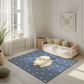 Kinderteppich "Samu Schäfchen" von spielzwerg. Ambientebild von einem hellen, freundlichen Kinderzimmer mit weißen Holzwänden und hellem Holzboden. In der Ecke steht ein niedriges Holzbett mit weißen Decken und hellgrünen Kissen. Davor liegt der Teppich. Links steht ein kleines Holzspielzeugrad am Fenster mit weißen Vorhängen. An der Wand hängt ein gerahmtes Bild mit einem dezenten, kreisförmigen Muster. RUG-00148-XL, RUG-00148-L.