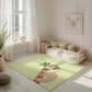 Kinderteppich "Flori Faultier" von spielzwerg. Ambientebild von einem hellen, freundlichen Kinderzimmer mit weißen Holzwänden und hellem Holzboden. In der Ecke steht ein niedriges Holzbett mit weißen Decken und hellgrünen Kissen. Davor liegt der Teppich. Links steht ein kleines Holzspielzeugrad am Fenster mit weißen Vorhängen. An der Wand hängt ein gerahmtes Bild mit einem dezenten, kreisförmigen Muster. RUG-00135-XL, RUG-00135-L.