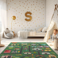 Spielteppich "Vorstadtchaos" von spielzwerg. Ambientebild von einem hellen Kinderzimmer mit weißem Holzboden und weißen Wänden, dekoriert mit goldenen Dreiecken und einem großen goldenen Buchstaben 'S'. Links steht ein gemütlicher Sessel mit Kissen und Decke, daneben eine goldene Stehlampe. In der Mitte liegt der Teppich. Rechts sitzt ein lachender Junge in einem weißen Spielzelt mit goldenen Punkten. Im Hintergrund ein schlichtes Bett mit weißer Decke und goldenen Akzenten. RUG-00104-XL, RUG-00104-L.