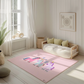Kinderteppich "Einhornfamilie" von spielzwerg. Ambientebild von einem hellen, freundlichen Kinderzimmer mit weißen Holzwänden und hellem Holzboden. In der Ecke steht ein niedriges Holzbett mit weißen Decken und hellgrünen Kissen. Davor liegt der Teppich. Links steht ein kleines Holzspielzeugrad am Fenster mit weißen Vorhängen. An der Wand hängt ein gerahmtes Bild mit einem dezenten, kreisförmigen Muster. RUG-00116-XL, RUG-00116-L.